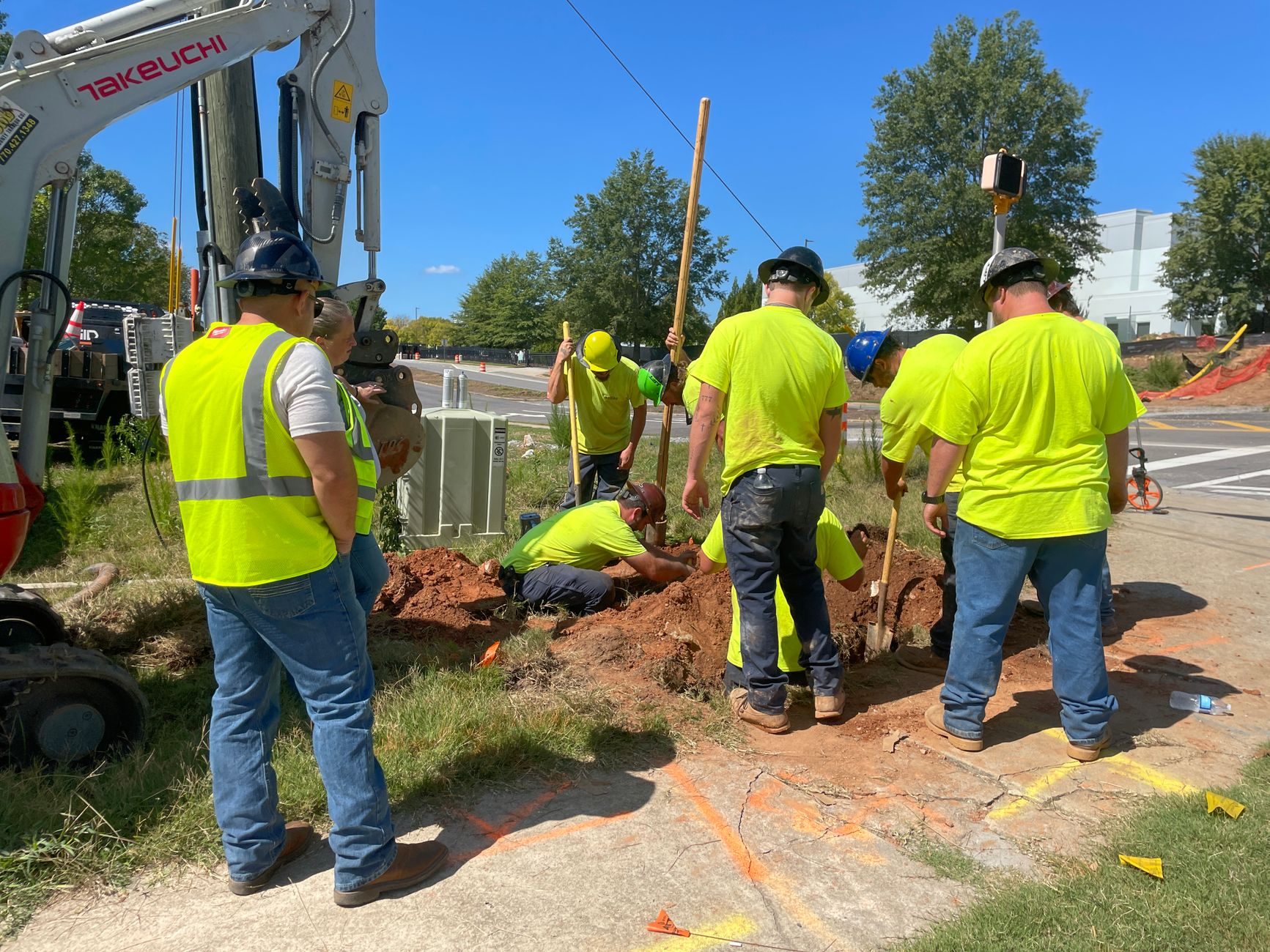 A crew in high-visibility vests at an excavation beside an excavator