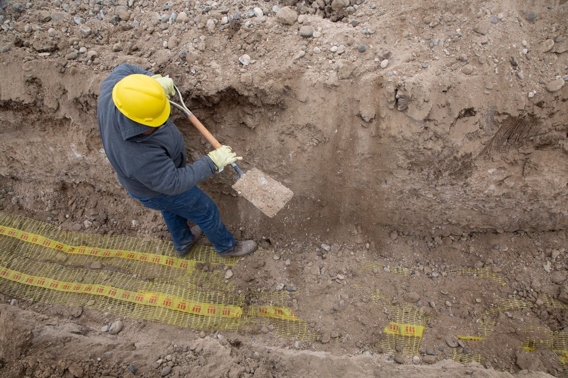 A worker in a hard hat digging by hand in a trench beside yellow locate marks