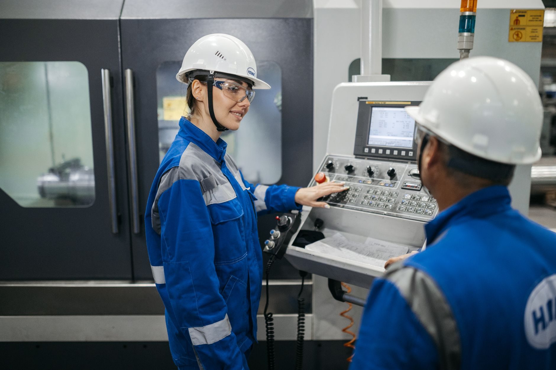 A supervisor showing a technician how to operate an industrial control panel