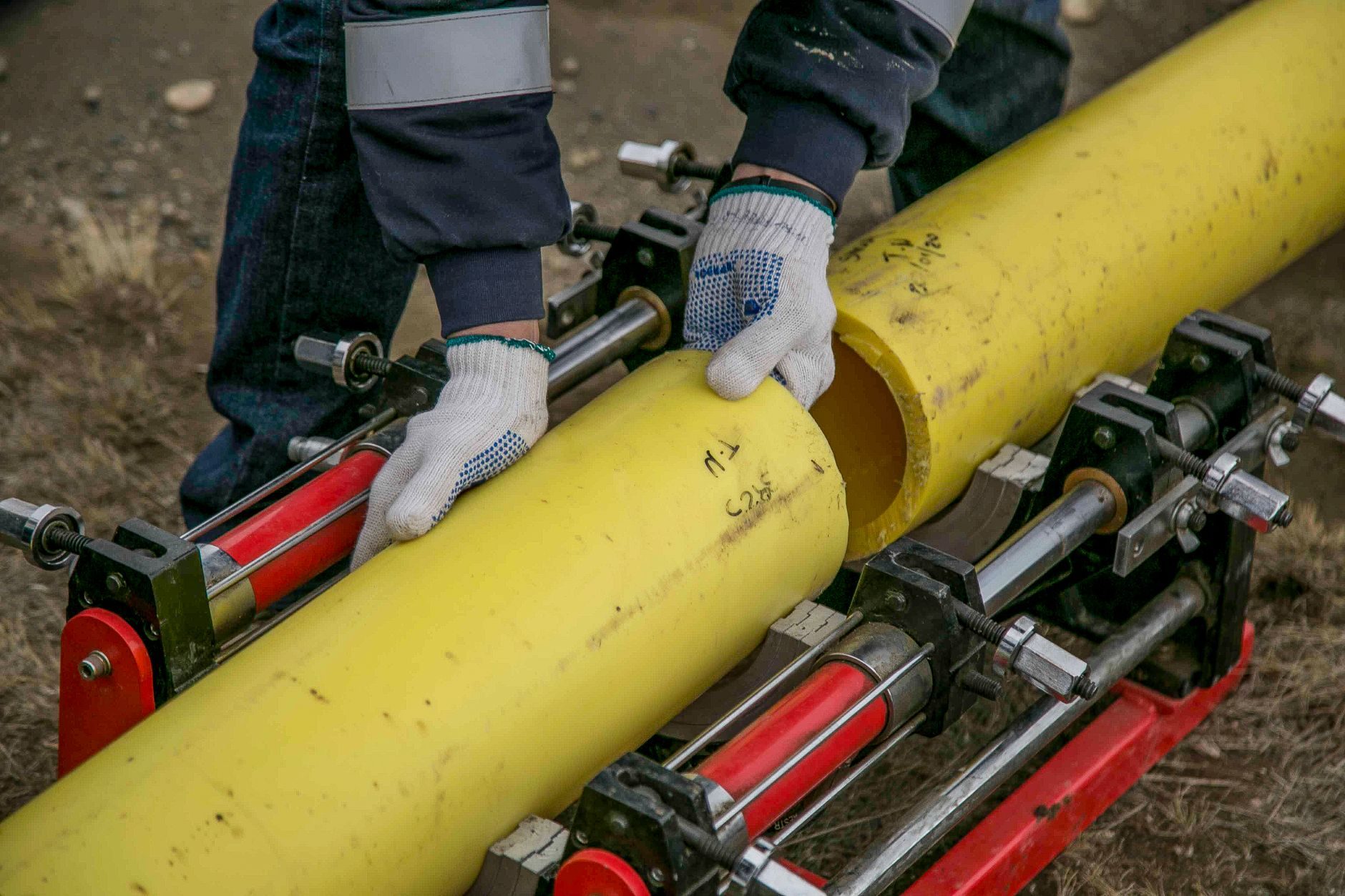 Gloved hands fitting a yellow polyethylene gas pipe into a fusion machine